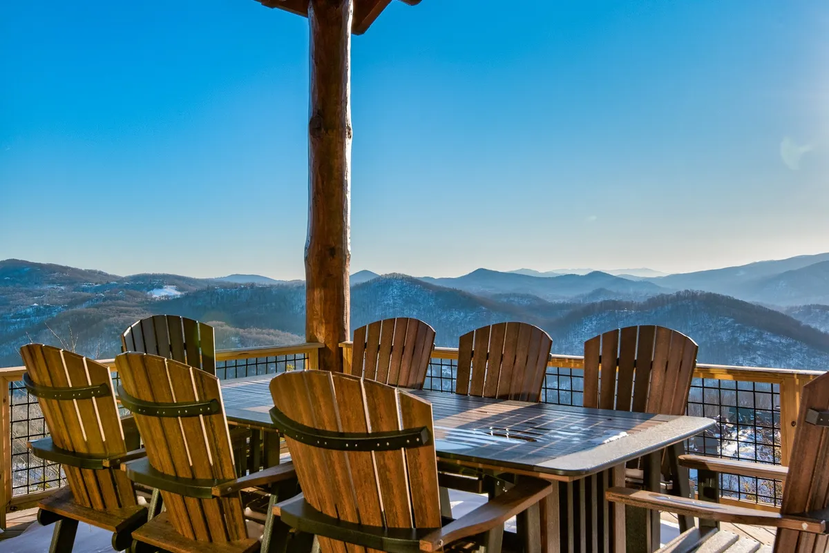 This exterior shot highlights a wooden dining table and Adirondack chairs on a deck overlooking sweeping mountain vistas. The setup suggests communal outdoor meals, relaxing conversations, and the enjoyment of fresh mountain air—perfect for family barbecues, gatherings, and watching events on the Great Lawn.