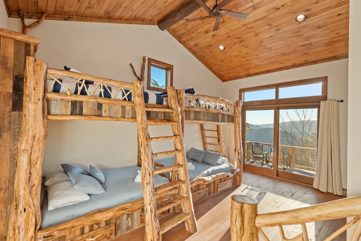 A cheerful and cozy bunk room with sturdy wooden bunk beds, large windows, and a wooden ceiling. The atmosphere is playful and inviting, perfect for children or the young at heart.
