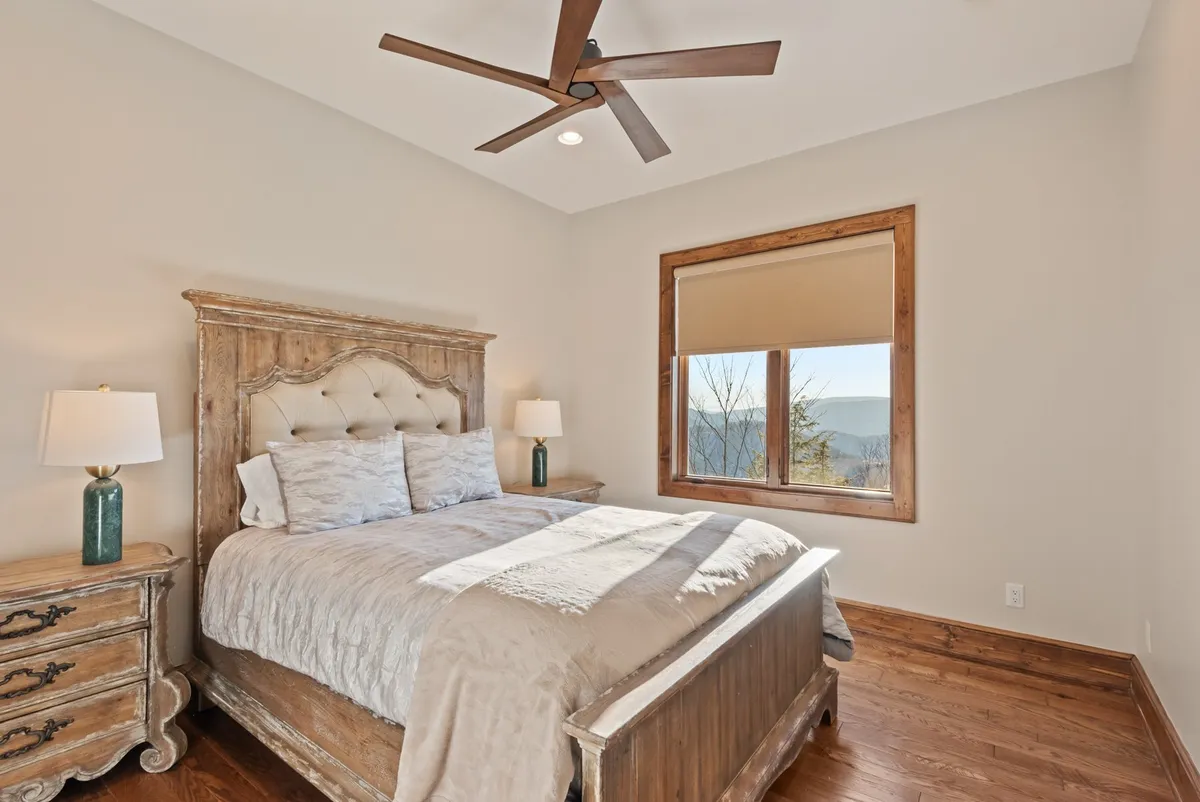 A queen bedroom with plush bedding, warm wooden furniture, and a window offering a serene view. The mood is comfortable and restful, perfect for unwinding after a day of adventure.