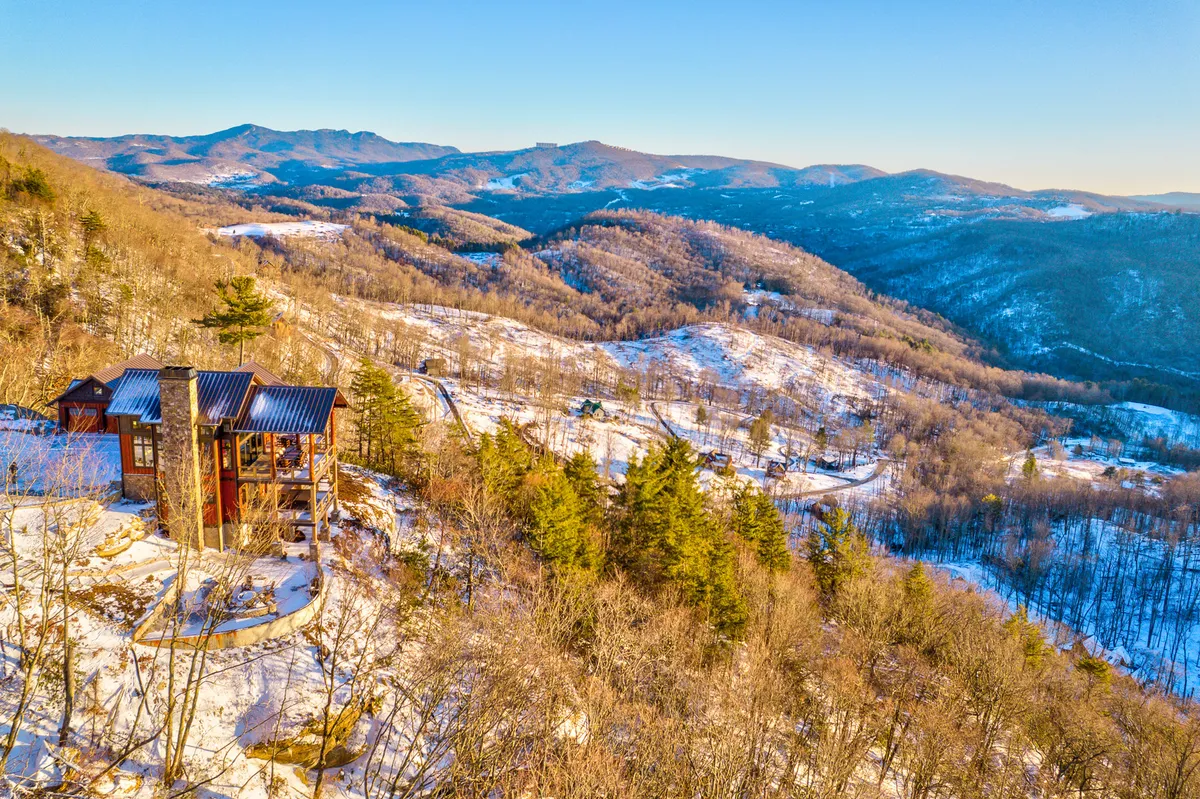 An expansive view of a mountainous landscape with a modern cabin nestled in the scene. Snow covers the ground, and the environment suggests opportunities for hiking, nature observation, and seasonal activities. The perspective draws attention to the proximity of natural attractions and adventure.