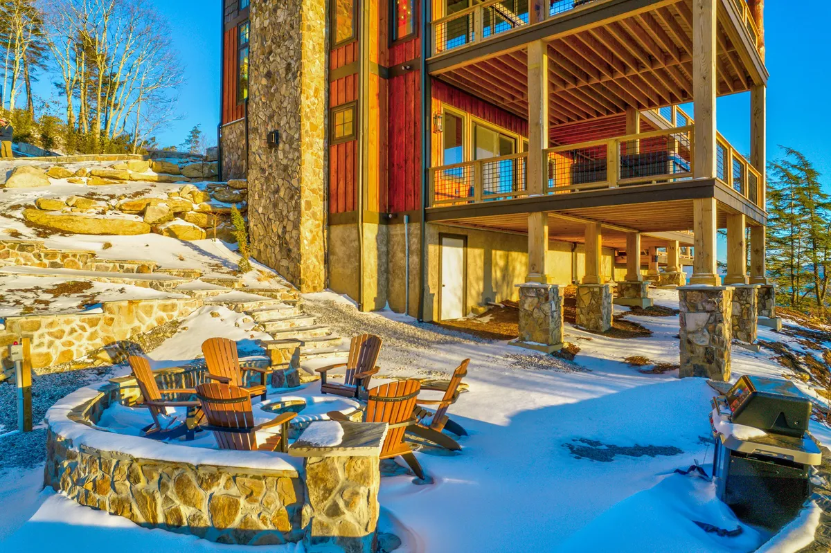 A built-in stone fire pit surrounded by Adirondack chairs on a snow-dusted ground, adjacent to a rustic wooden structure. The space feels inviting for evening gatherings, stargazing, and sharing stories around the fire.