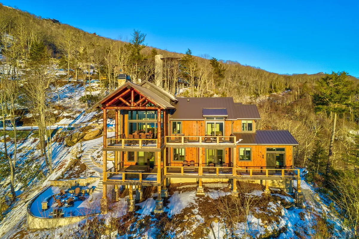 A view of a large wooden structure with expansive glass windows and balconies, surrounded by snow-covered ground and tall trees. The scene suggests a welcoming gathering place for families, positioned amid scenic mountains. The outdoor setting is tranquil, with hints of adventure and exploration available right outside the door.