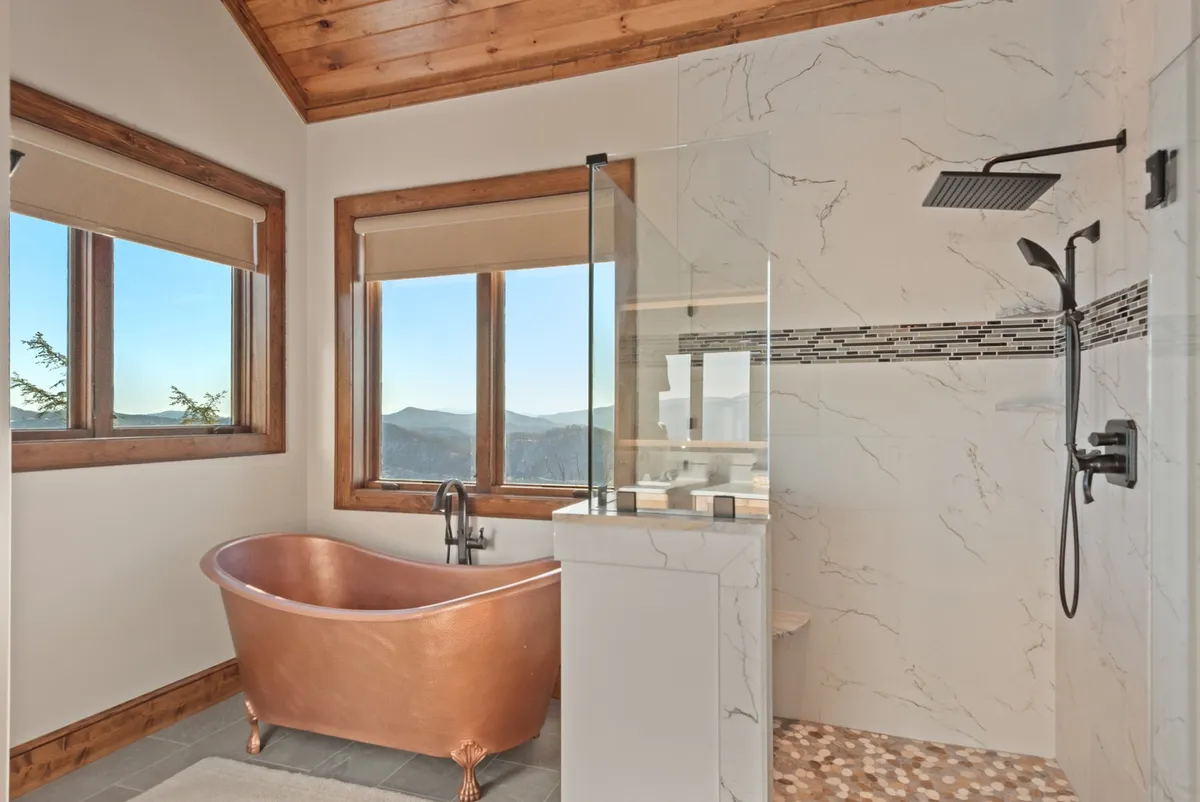 This image features a luxurious copper bathtub positioned by large windows that offer stunning views of the mountains, as well as a modern shower with spa-like details. The scene is tranquil and exudes a sense of relaxation and indulgence.