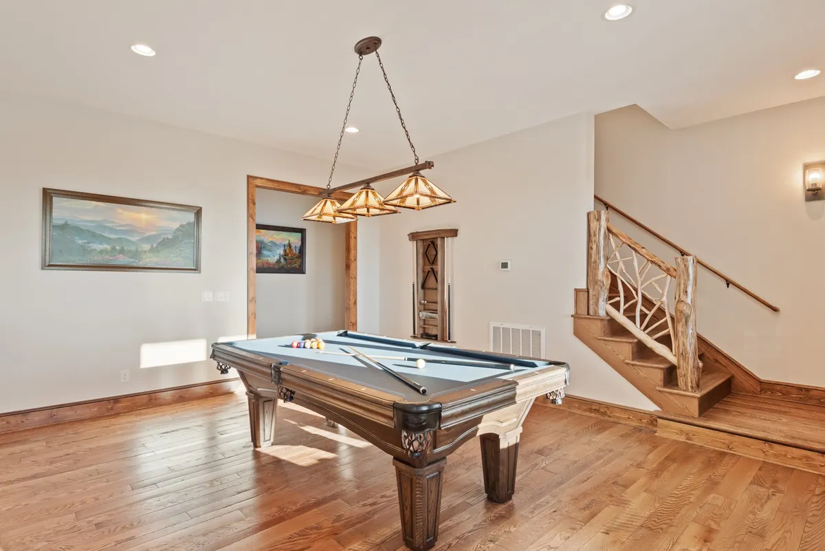 A stylish, well-lit game room featuring a pool table under a chandelier, artwork on the walls, and a staircase leading to another level. The layout feels open and social, emphasizing the room’s recreational purpose while highlighting the attractive design elements.